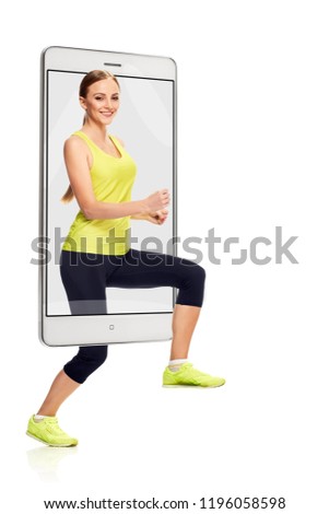 Attractive positive sporty woman running on white background, concept virtual reality of the smartphone. going out of the device