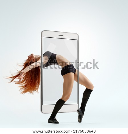 Slim athletic woman showing gymnastic elements while dancing, concept virtual reality of the smartphone. going out of the device