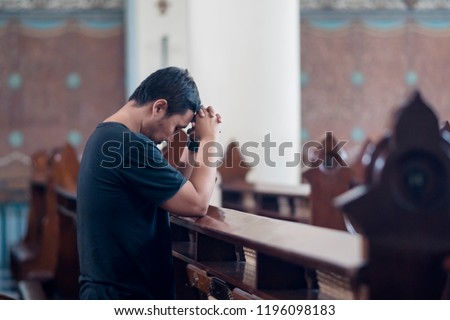 Picture of young man standing with clasped hands while praying to GOD in the church