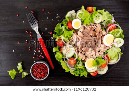 Salad with tuna, anchovies and vegetables. Mediterranean food. The background is black. Top view. Copy space. Horizontal shot.