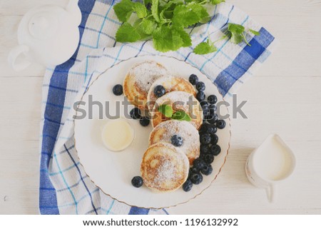 Pancakes on a white plate with condensed milk, blueberries and melissa