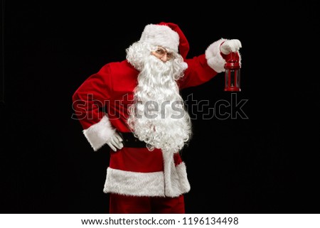 Christmas concept. Santa Claus holds a lantern in his hand and looks into the camera on a black background. Royalty-Free Stock Photo #1196134498