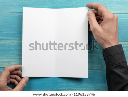 Mens hands holding empty white booklet on blue wooden background. View from above
