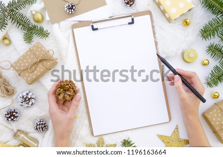 Flat lay clipboard mockup. Woman's hands holds black brush pen and pine cone. Blank white paper sheet mock up. Winter holidays mood for hand lettering. Merry christmas happy new year. Flatlay