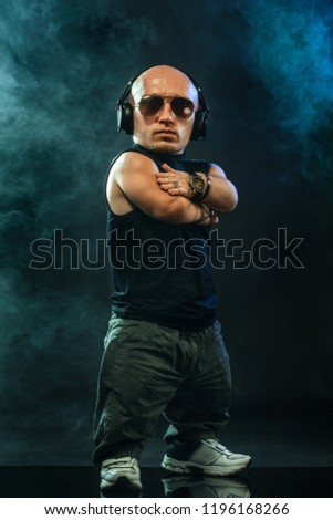 Portrait of stylish midget MC in with headphones and sunglasses posing with microphone. Royalty-Free Stock Photo #1196168266