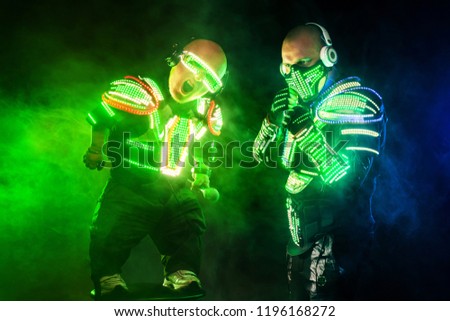 Mysterious man and midget in black wear, neon mask and gloves. Character pastors or wizards in robe from the future. Assassin with strong face expression. Fantasy book or computer game cover concept. Royalty-Free Stock Photo #1196168272