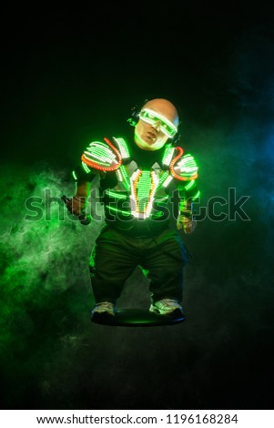 Little man, dwarf. Mysterious midget in black wear, neon mask and gloves. Character pastor assassin or wizard in robe from the future. Fantasy book or computer game cover concept. Royalty-Free Stock Photo #1196168284