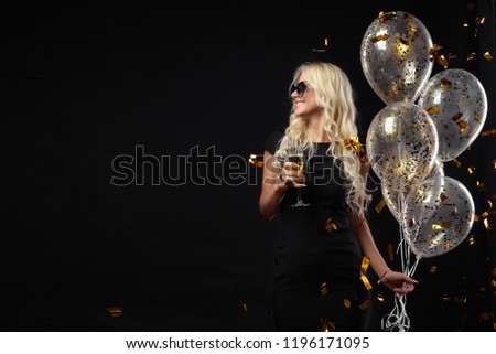 Brightfull expressions of happy emotions of  amazing blonde girl celebrating party on black background. Luxury black dresses, smiling, a glass of champagne, golden tinsels,  balloons, long curly hair Royalty-Free Stock Photo #1196171095