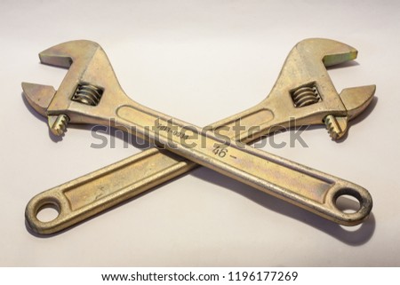 Large adjustable wrenches of golden color are crossed, on a white background.