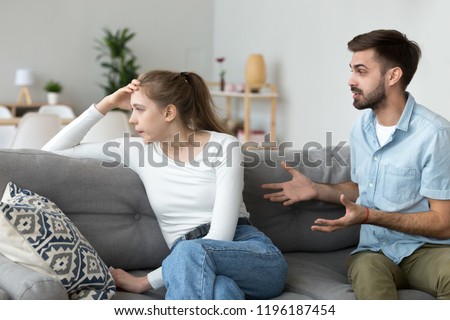 Unhappy young millennial married couple sitting on couch in living room at home and quarrelling. Husband arguing emotionally talking frustrated wife looking away. Break up and misunderstanding concept Royalty-Free Stock Photo #1196187454