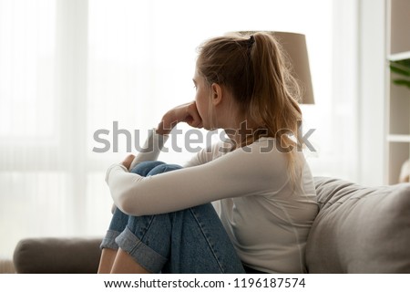 Side view young woman looking away at window sitting on couch at home. Frustrated confused female feels unhappy problem in personal life quarrel break up with boyfriend or unexpected pregnancy concept Royalty-Free Stock Photo #1196187574