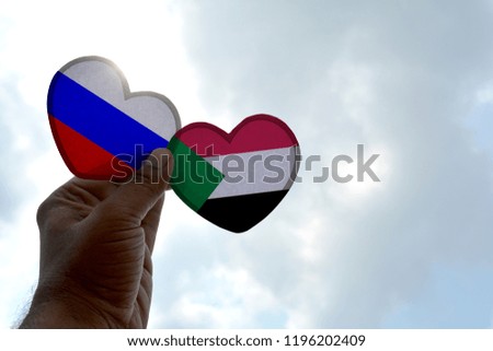 Hand holds a heart Shape Russia and Sudan flag, love between two countries
