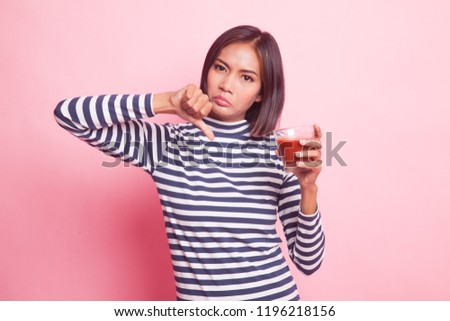 Young Asian woman  thumbs down hate tomato juice on pink background