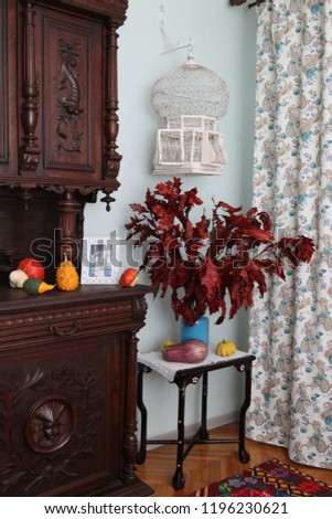 Bouquet of red autumn leaves and decorative mini pumpkins. Bohemian (boho) interior in retro style, antique bird's cage, antiquarian buffet. Interior design, decor. Autumn (fall) still life at home