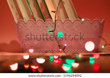 Books in basket and garland on pink background. Garland lights bokeh in the foreground.