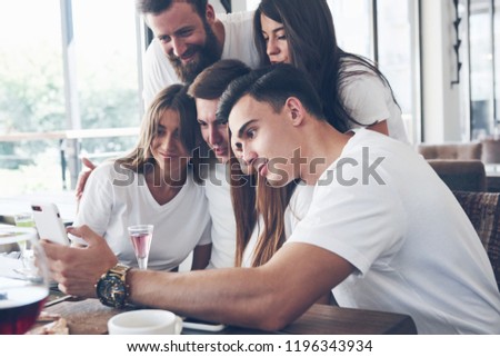 A group of people make a selfie photo in a cafe. The best friends gathered together at a dinner table eating pizza and singing various drinks.