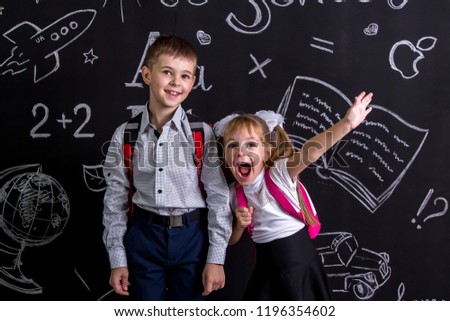 Excited and cheerful schoolkids standing before the chalkboard as a background with a backpack on his back showing happy emosions. Landscape picture.