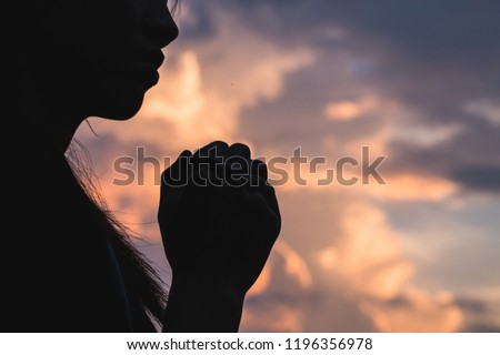 Silhouette off   young woman praying for God's blessings with the power and power of the sacred On the background of sunrise. The concept of God and spirituality. Royalty-Free Stock Photo #1196356978