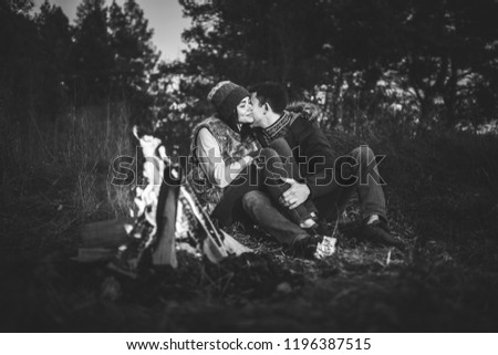 Pretty young couple relaxing near bonfire in the forest at evening time