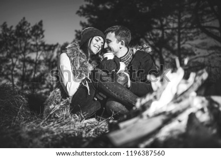 Pretty young couple drinking hot beverage in the forest near bonfire