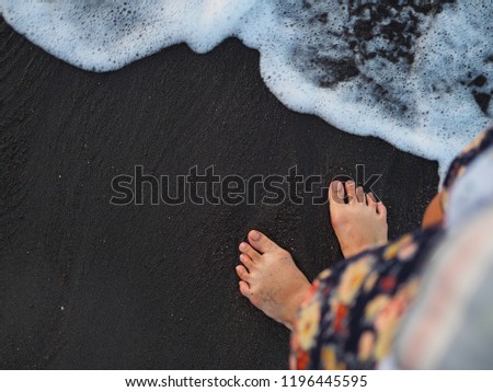 Barefoot Stand alone on the beach at Amed beach Bali. With black sand and wave breaking.