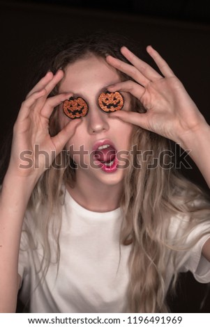 Portrait of beautiful young shocked surprised excited woman posing isolated over dark beige background wall holding pumpkin halloween glitter decor in hands covering eyes.