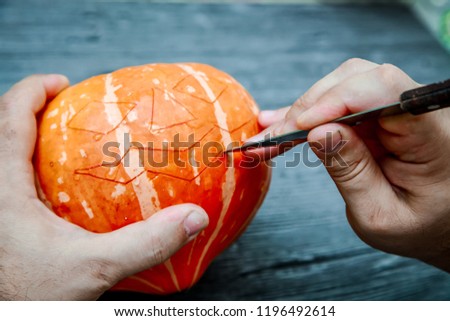 Men's hands with knife cut out pumpkin mask for Halloween