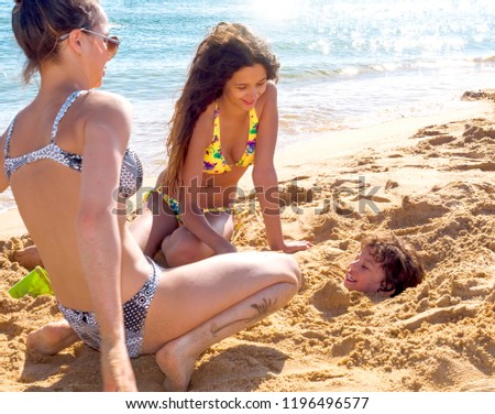 Caucasian brother and two sisters playing buried in sand at beach