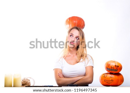 Halloween concept, Girl sitting at table with pumpkins preparing for holiday with candle and rope, thinking how to do Jack lantern, funny or spooky pumpkin on head. Trick or treat tradition