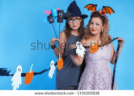 Friends are preparing for Halloween. Two women in masquerade dresses. Funny witches posing in the studio.