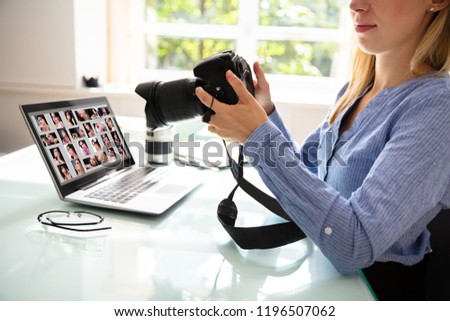 Female Editor Holding DSLR Camera With Laptop On Desk