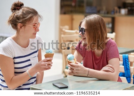 People, lifestyle and rest concept. Joyful hipsters have spare tine, eat delicious ice cream in cafe during summer, wear sunglasses, tell each other anecdotes, being in good mood, have nice relations