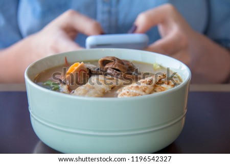 Millennial girl is chatting during lunch time on smartphone in front of bowl of chicken soup