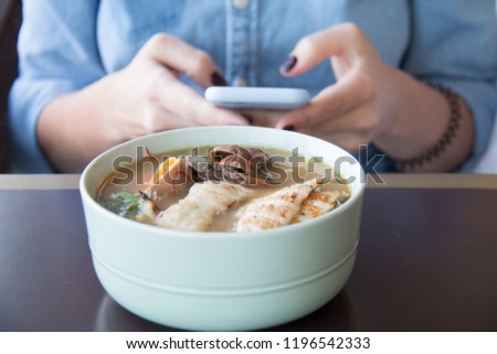Millennial girl is chatting during lunch time on smartphone in front of bowl of chicken soup