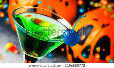 Halloween composition with festive drink, green cocktail and pumpkins lanterns and fallen leaves on night dark blue background, selective focus