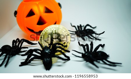 Bitcoin golden coin with plastic spiders and a plastic pumpkin baskets for trick and treat. White background