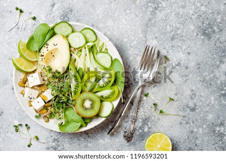 Vegan, detox Buddha bowl with quinoa, avocado, zucchini noodles, cucumber, tomato, lime, kiwi, tofu, spinach, micro greens, pepitas. Grey concrete background