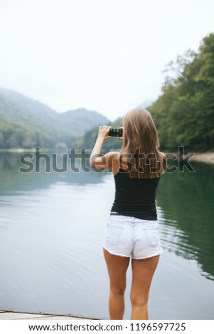 girl in white shorts takes pictures on the smartphone lake