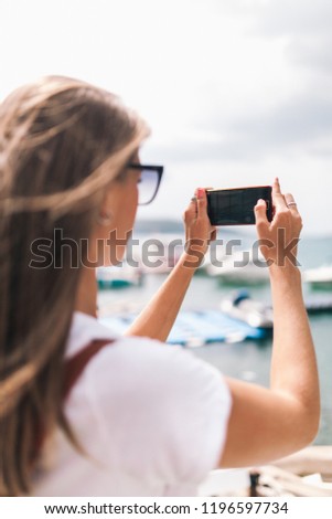 beautiful girl with a striped backpack takes pictures on the phone a beautiful landscape on the coast of Montenegro
