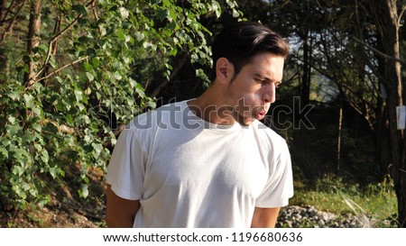 Young rude handsome man standing in nature, spitting on the ground Royalty-Free Stock Photo #1196680636