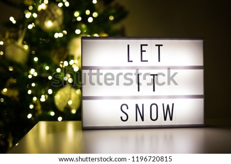 winter and first snow concept - lihtbox with text let it snow in dark room with decorated christmas tree