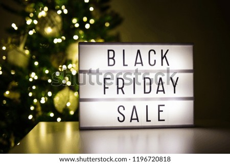 winter shopping and sale concept - lihtbox with text black friday sale in dark room with decorated christmas tree