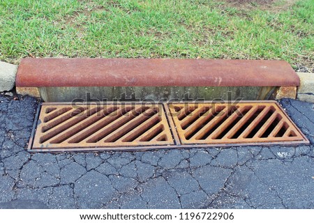 Rusted iron grate over a storm drain along the road