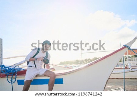 Photography and travel. Young man with rucksack holding camera enjoying beautiful tropical sea view on fishing beach.