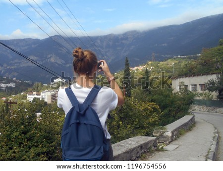           young girl on vacation by the sea taking pictures of the mountains