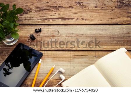 Work table with smartphone screen, open notebook ang green leaves. Copy space. Rustic background.