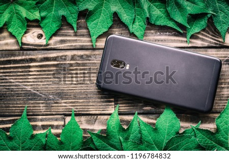 Black Smartphone and green Leaves on wood background texture.