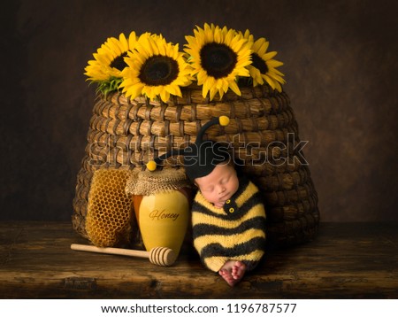 Cute baby in bee outfit sleeping against antique beehive