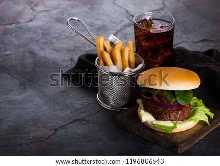 Fresh beef burger with sauce and vegetables and glass of cola soft drink with potato chips fries on stone kitchen background.