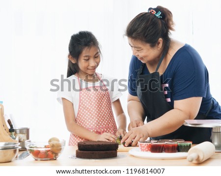 Young Asian kid with her mom making handmade chocolate cake in the kitchen together in holiday.